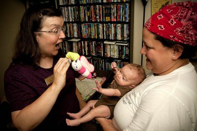 Nurse slowing a toy to a baby in their mother's arms