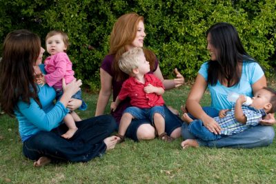 Three mothers sitting on the grass with their young children